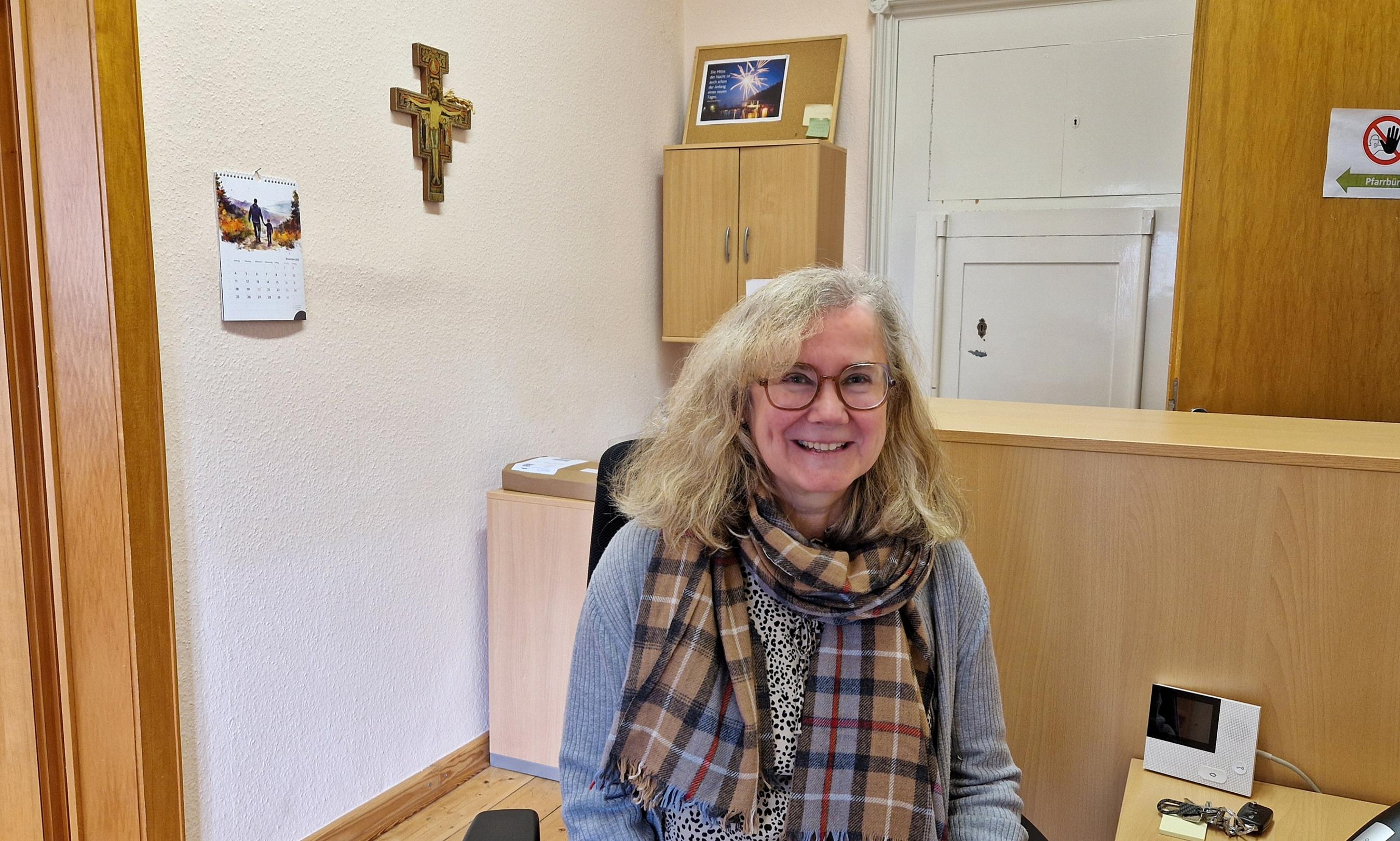 Pfarrsekretärin Barbara Stutzer im Büro, im Hintergrund ein Kreuz