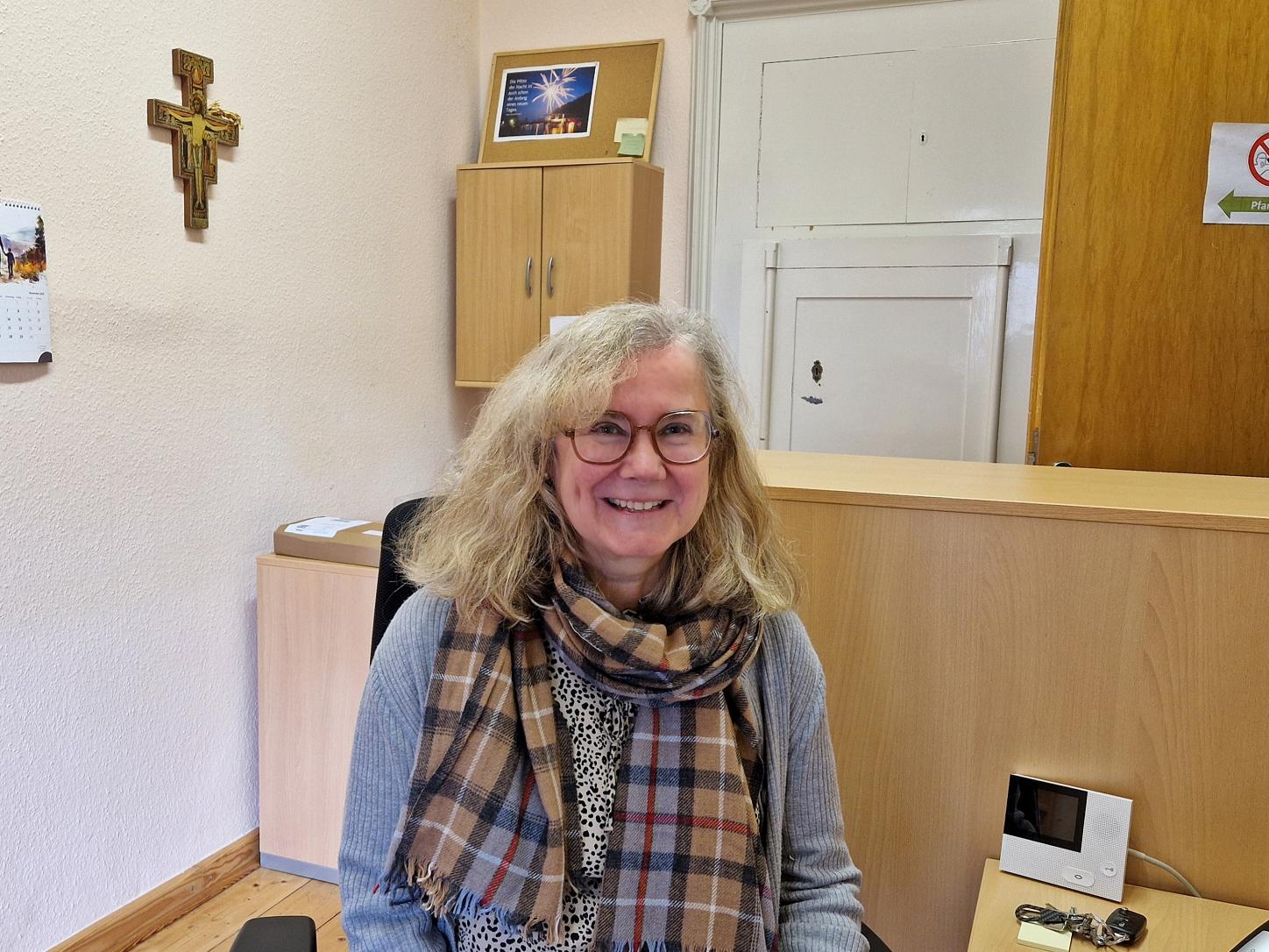 Pfarrsekretärin Barbara Stutzer im Büro, im Hintergrund ein Kreuz