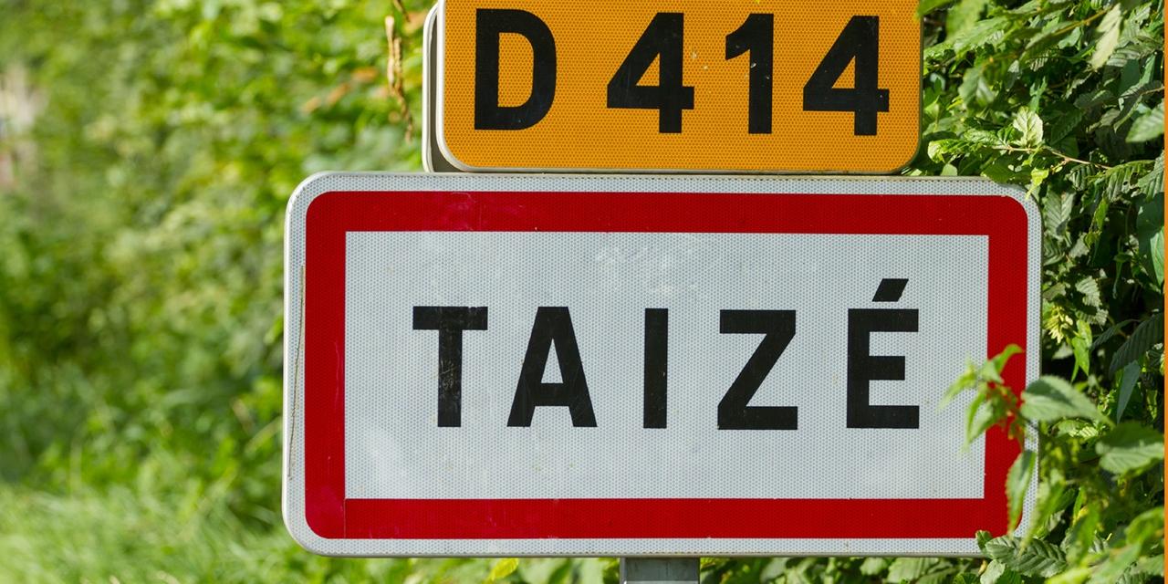 Straße D414 mit Ortsschild von Taize im Hintergrund Blätter und Wiese