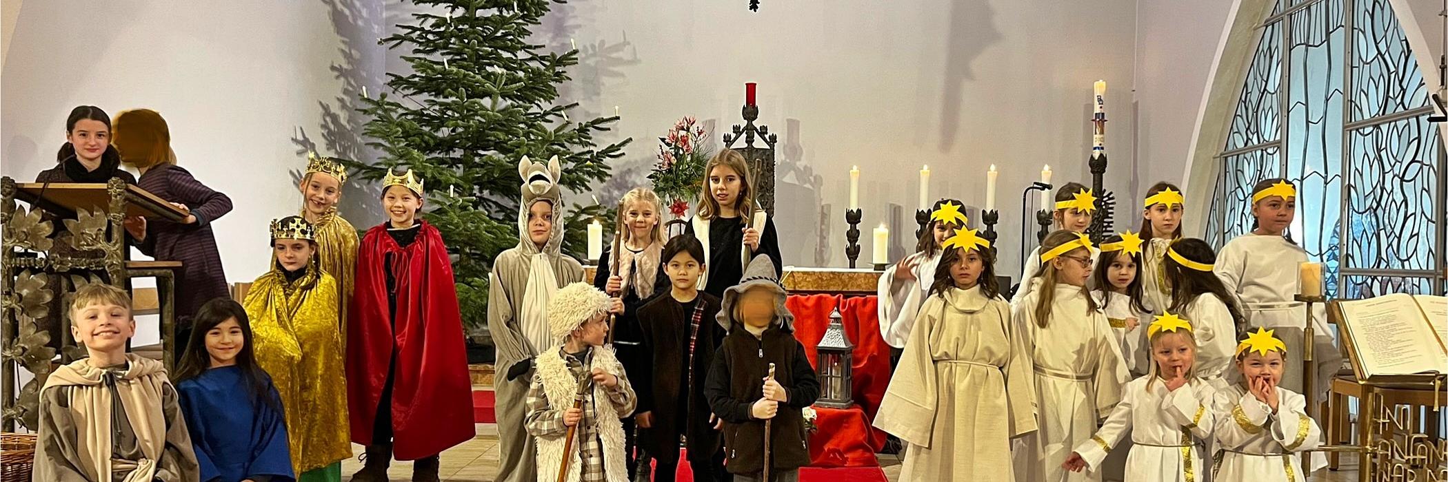 Kinder als Darsteller eines Krippenspiels gekleidet stehen im Altarraum einer Kirche, rechts eine Gruppe Engel, links und in der Mitte die Hirten, Tiere und die Heilige Familie. Im Hintergrund ein Weihnachtsbaum und ein Kreuz (c) Isabel Weiher für Pfarrei Koblenz St. Beatus Kinder als Darsteller eines Krippenspiels gekleidet stehen im Altarraum einer Kirche, rechts eine Gruppe Engel, links und in der Mitte die Hirten, Tiere und die Heilige Familie. Im Hintergrund ein Weihnachtsbaum und ein Kreuz