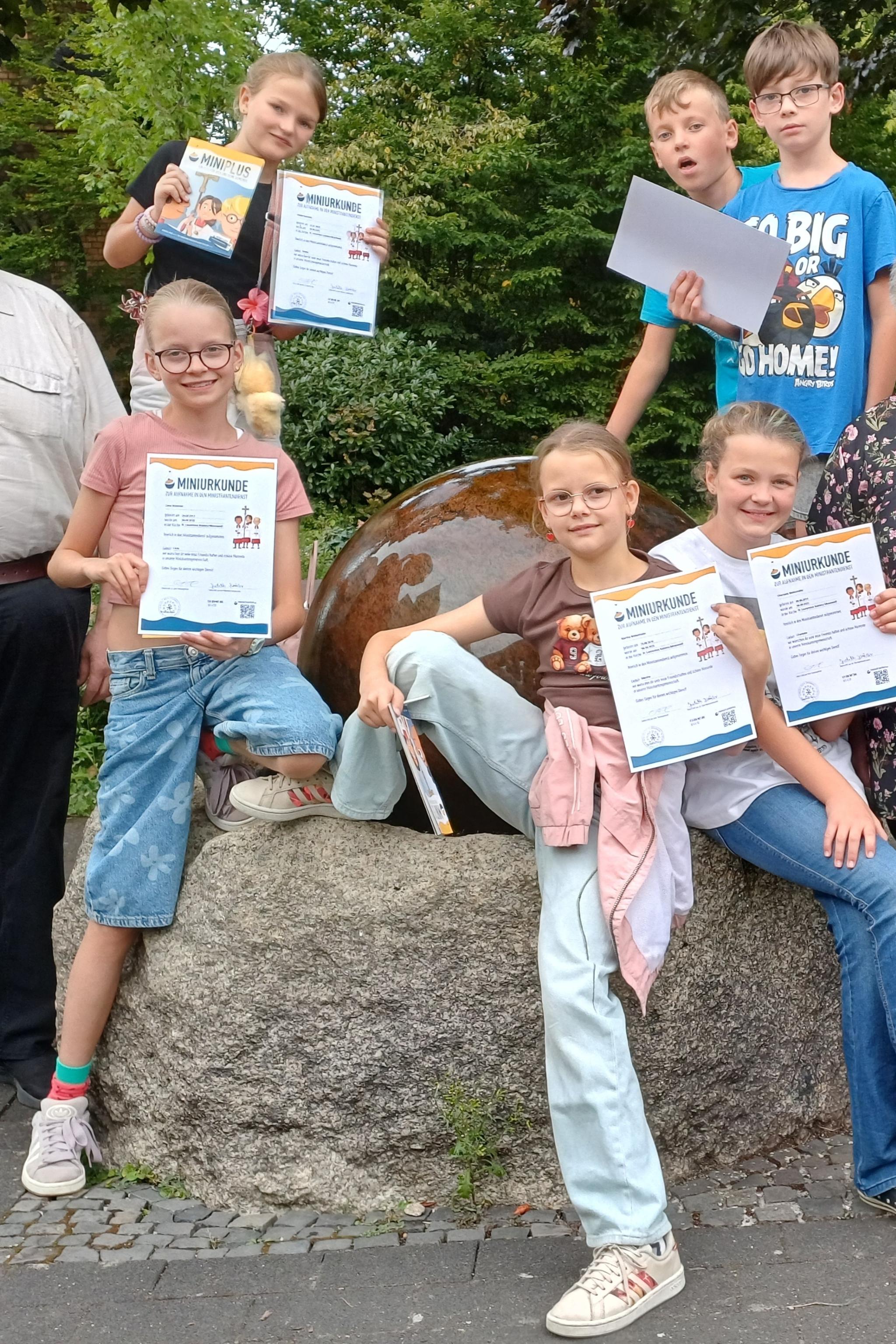 in der Mitte sechs Kinder, die eine Urkunde hochhalten, rechts und links stehen ein Mann und eine Frau