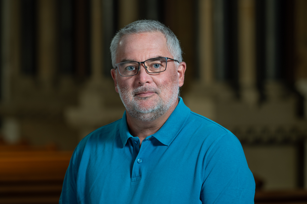 Portraitfoto Mann im blauen Polohemd vor dunklem Hintergrund