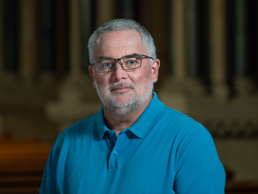 Portraitfoto Mann im blauen Polohemd vor dunklem Hintergrund