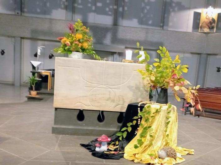 Altar in der St. Franziskuskirche mit Sonnenblumen geschmückt davor ein Tisch, bedeckt mit einem schwarzen und gelben Tuch, darauf eine Vase mit herbstlichen Zweigen. Um die Vase ein großer Rosenkranz gelegt