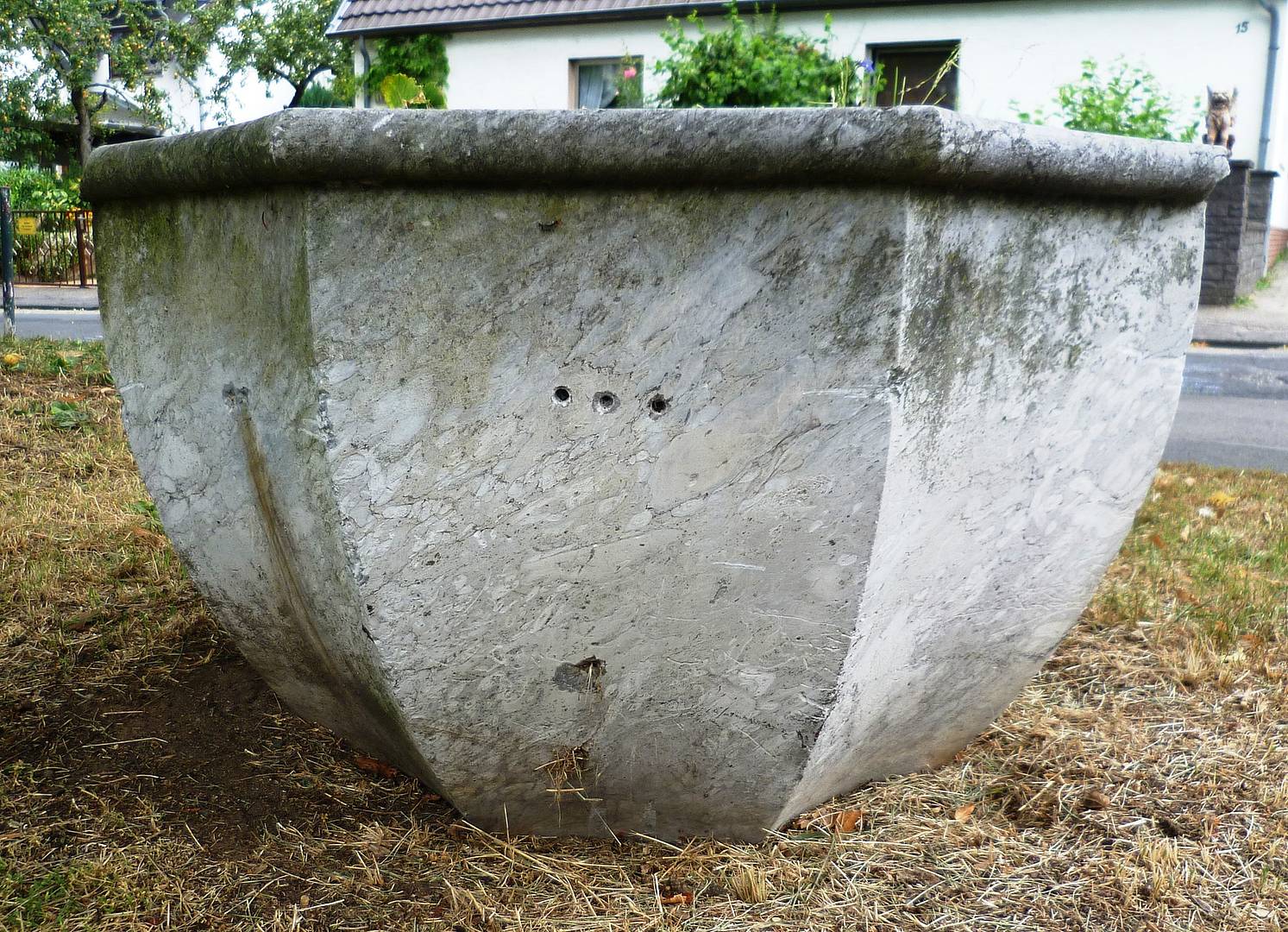 Der Taufbrunnen steht auf der Wiese, ist verwittert und sieht restaurierbedürftig aus