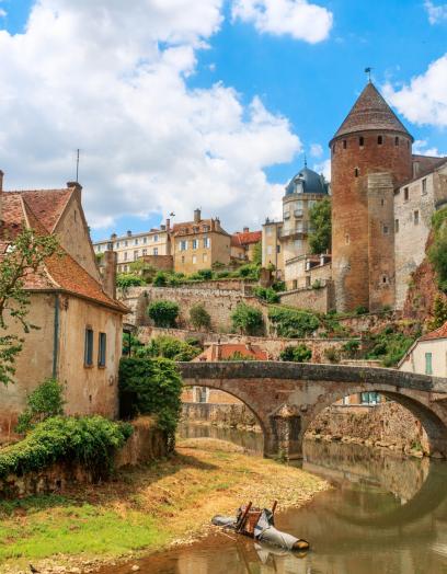 Zu sehen ist ein Ansicht der Stadt Semur, die beidseitig an einem Fluss liegt über den eine mittelalterliche Brücke führt. Idylisch, malerisch sind mittelalterliche Gebäude und prominent ein Turm zu sehen.