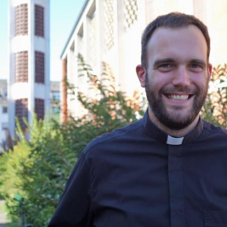 Jugendpfarrer Dominic Lück neben der Kirche St. Elisabeth im Hintergrund der Kirchturm